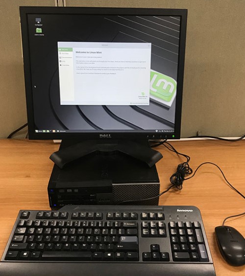 Computer CPU with monitor on top, keyboard and mouse. Monitor shows welcome screen of Linux Mint operating system.