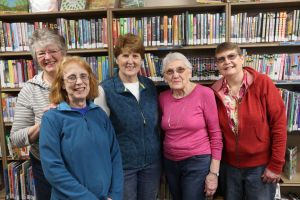 Five smiling women posing in front of a bookcase