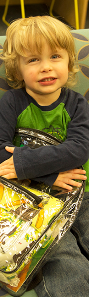 Child holding raising reader backpack smiling at the viewer.