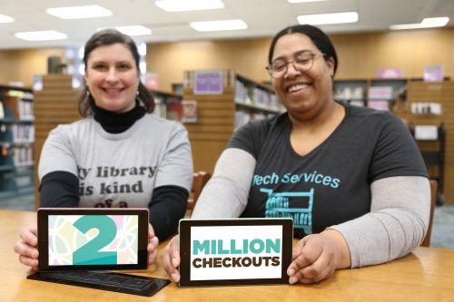 Thais (left) and Jessica (right) sit at a desk and each hold a Kindle eReader with the words 2 Million Checkouts on the screen.