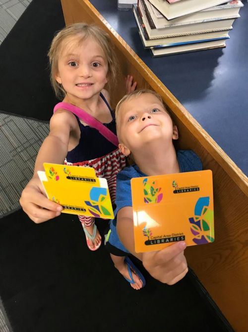 Two young blonde children hold library cards